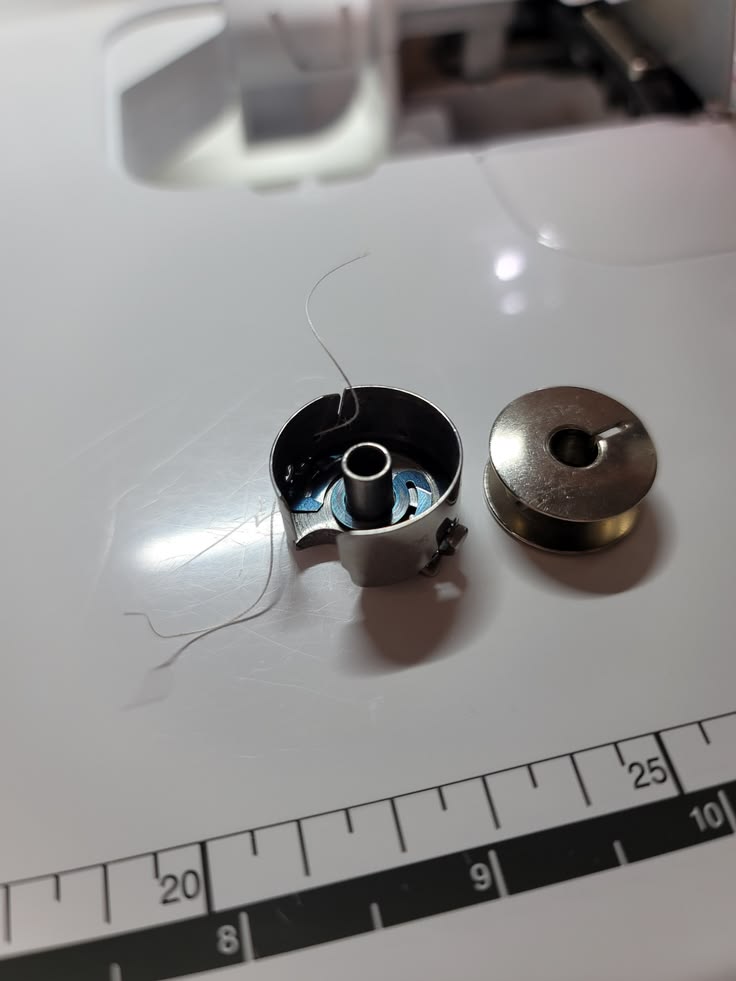 Close-up of the bobbin area: bobbin removed, hand wiping inside the bobbin case, thread visible caught in the tension spring