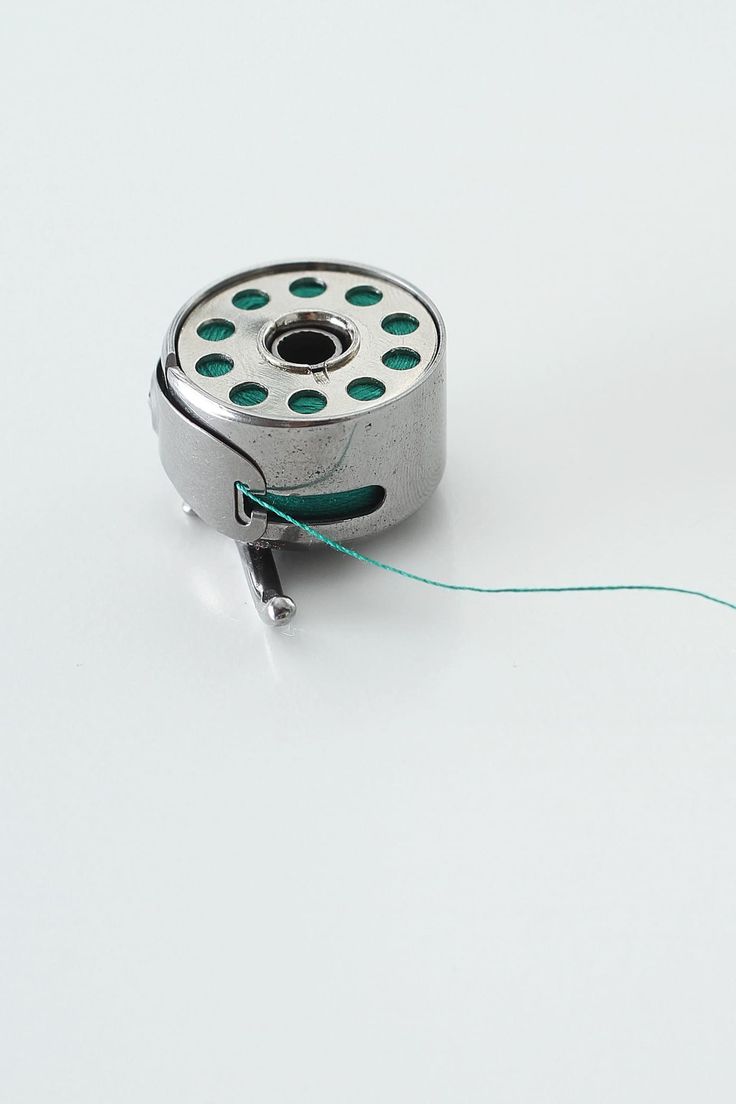 Overhead close-up of bobbin correctly loaded, thread being drawn beneath the tension spring with the thread path clearly visible