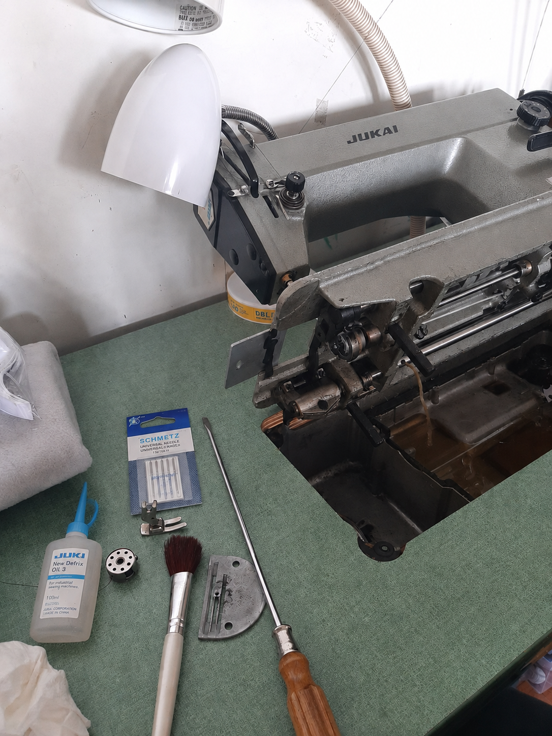 Flat-lay of three tools representing the three phases: a cleaning brush for Reset, a packaged needle for Restore, and a bottle of sewing machine oil for Protect