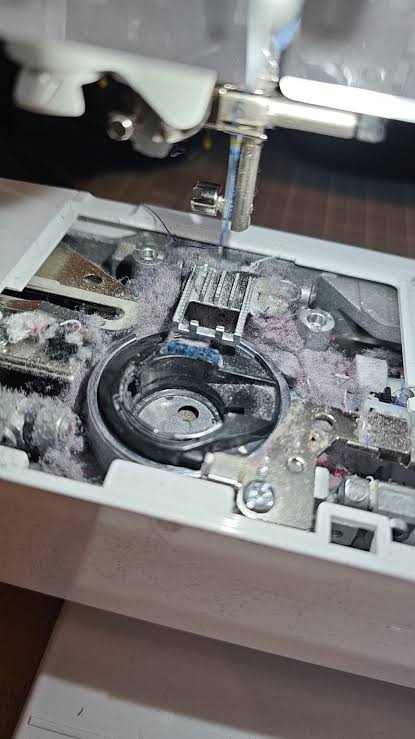 Close-up of lint packed into the feed dogs and needle plate area of a sewing machine, showing how fibre accumulates after regular sewing use