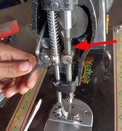 Close-up photograph of a sewing machine needle bar — the vertical metal rod that moves the needle up and down