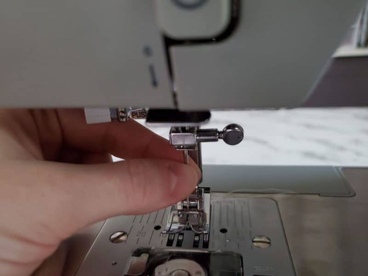 Close-up of a fresh needle being inserted into the needle clamp, flat side toward the back, with the clamp screw visible