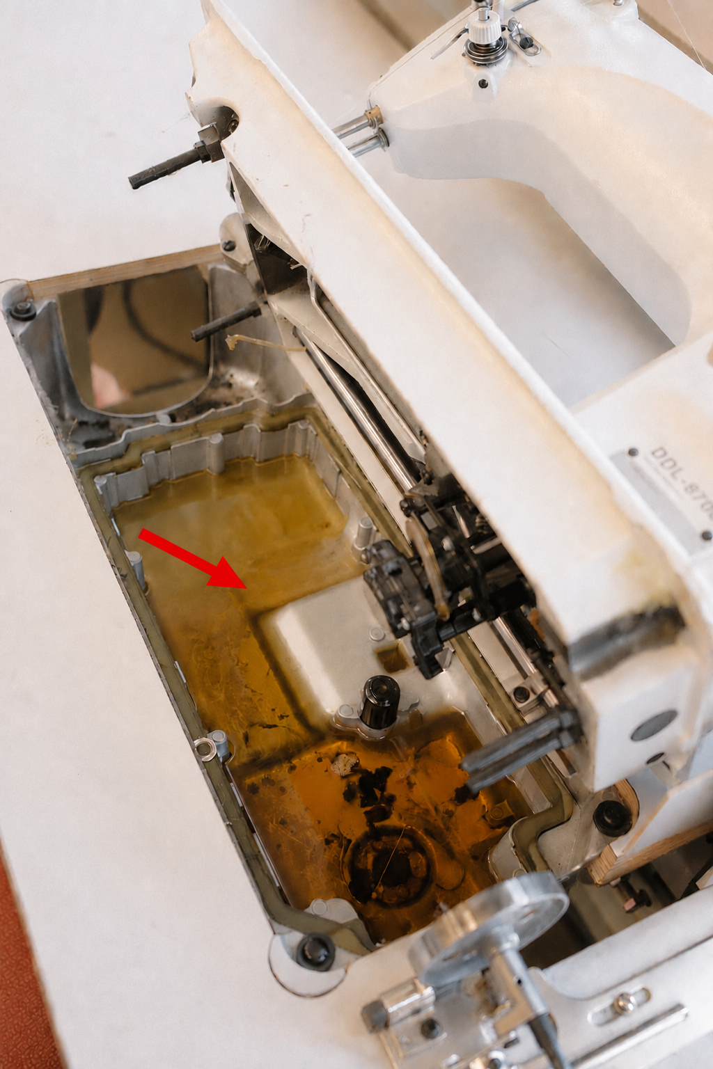 Close-up of the oil reservoir window on an industrial sewing machine arm, finger pointing to the minimum oil level line