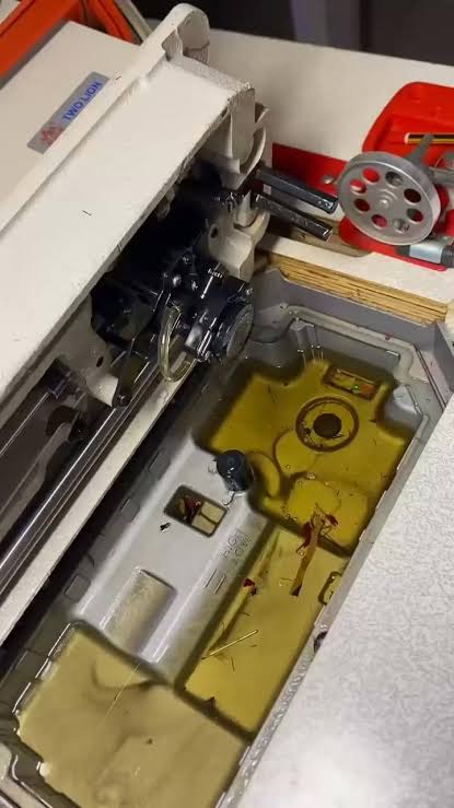 Close-up of an industrial sewing machine's transparent oil reservoir window, showing minimum and maximum oil level markings with clear amber-coloured oil at the correct level