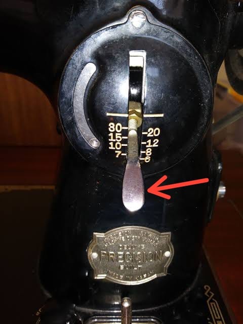 Close-up photograph of a sewing machine reverse lever or button on the machine face