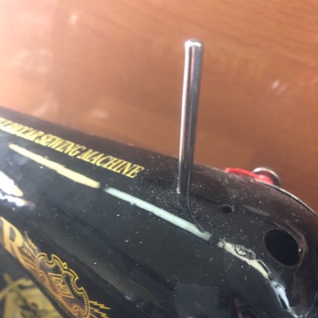 Close-up photograph of a sewing machine spool pin with a thread spool correctly mounted on it