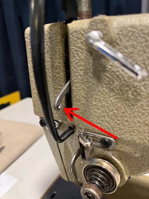 Close-up photograph of a sewing machine take-up lever — the moving arm on the front of the machine that pulls thread upward