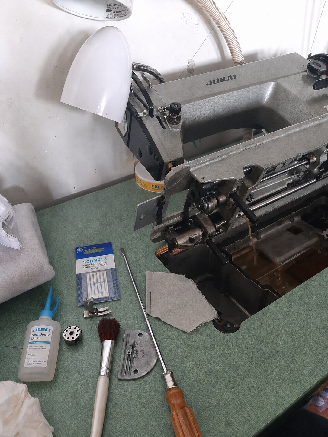 Flat-lay of tools needed for the weekly 5-minute sewing machine maintenance routine: lint brush, dry cloth, screwdriver, sewing machine oil, spare needle, and scrap fabric